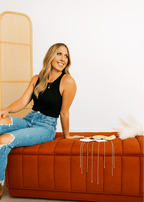 Woman sitting on a brown bench with a white wall and wooden rack in the background