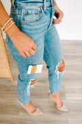 Close-up of a person wearing ripped blue jeans with a visible brand tag.
